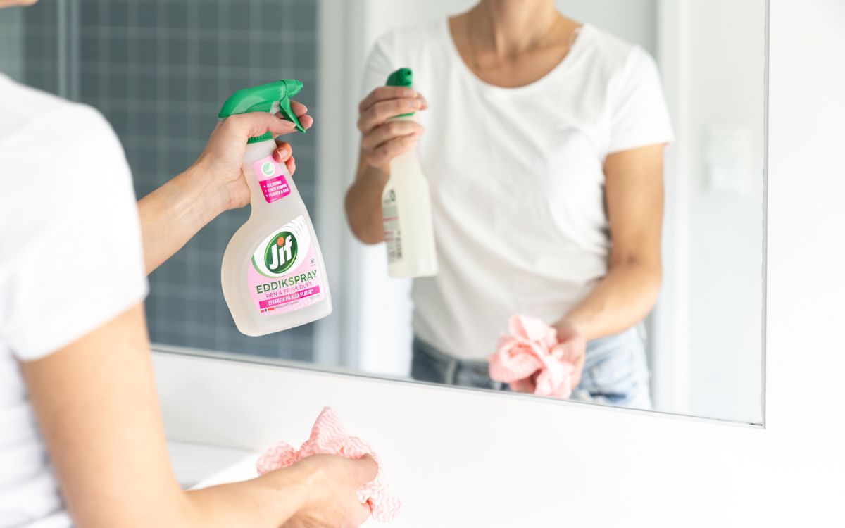 Kvinne vasker speil med Jif Eddik Spray.